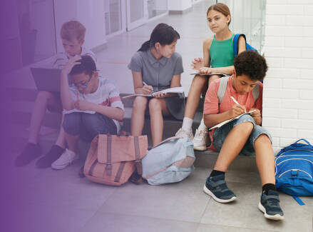 Five students sitting on steps doing schoolwork with their backpacks